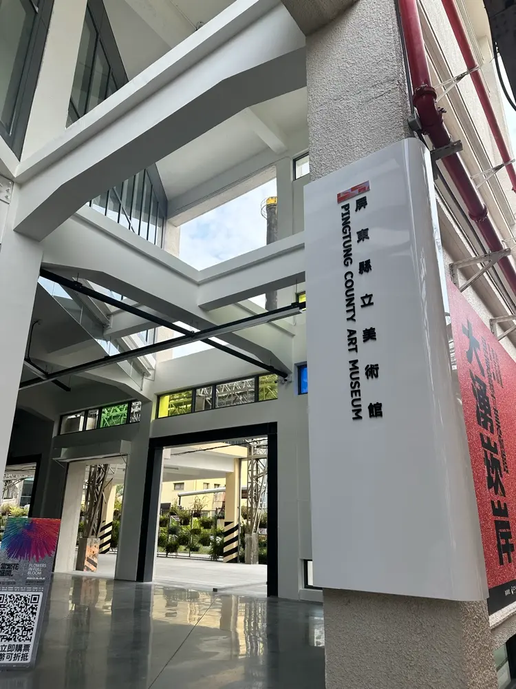 屏東縣立美術館入口處，保留了舊菸廠挑高的工業風鋼骨結構與純白牆面設計